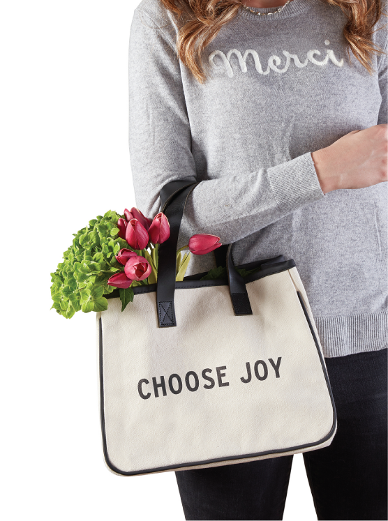 photo of person wearing grey shirt printed with word Merci, holding a shopping tote with words CHOOSE JOY